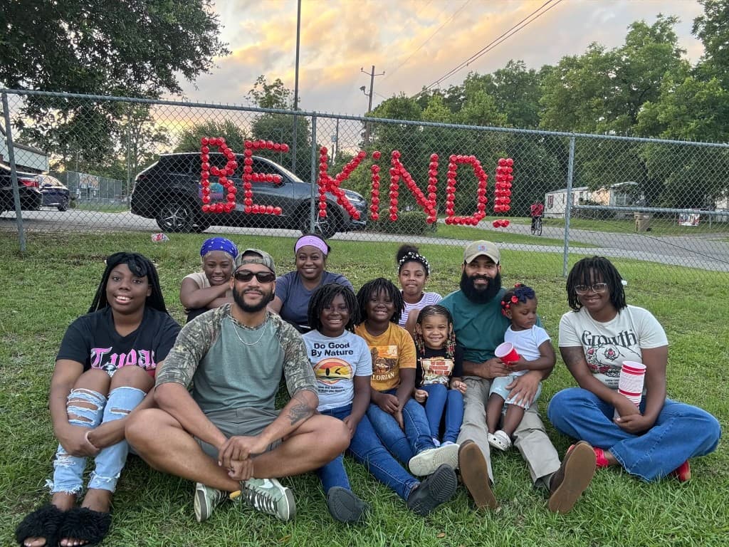 Families at sunset in front of a fence with BE KIND spelled in red cups