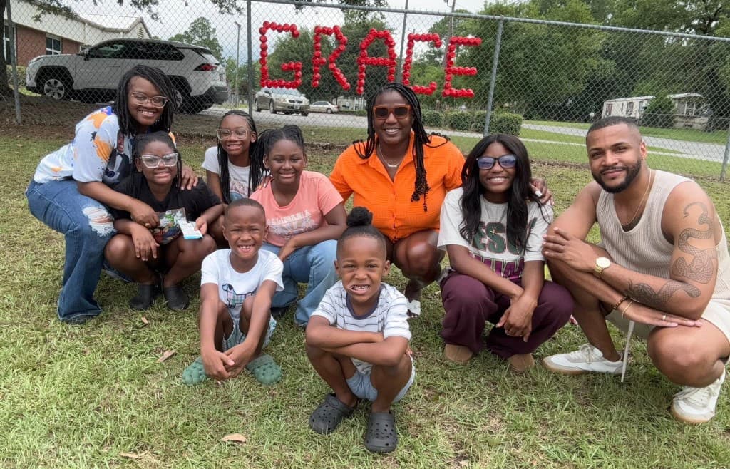 Families posing in front of a fence with GRACE spelled in red cups