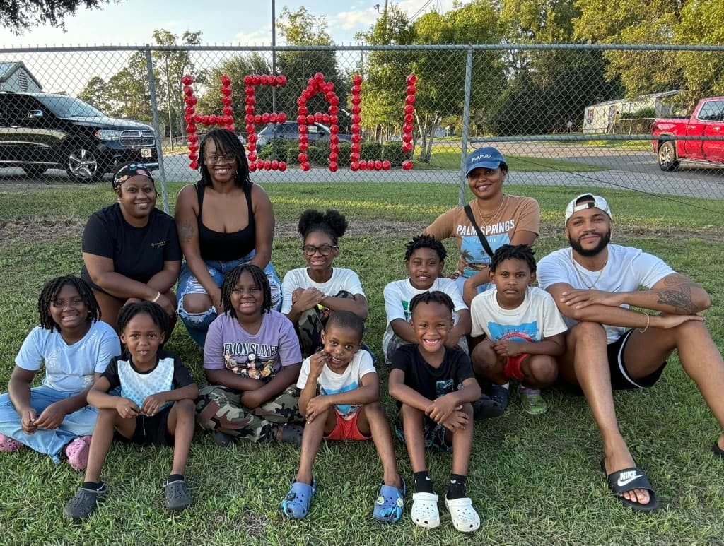Children and adults in front of a fence with HEAL spelled in red cups