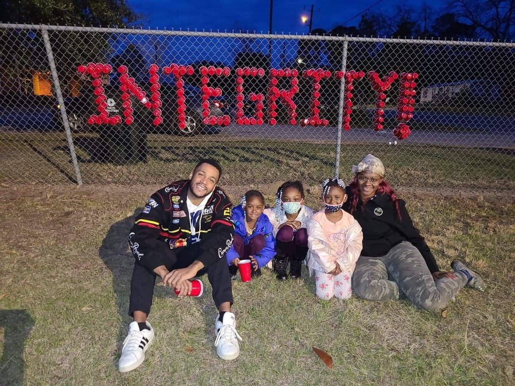 Group at night in front of a fence with INTEGRITY spelled in red cups