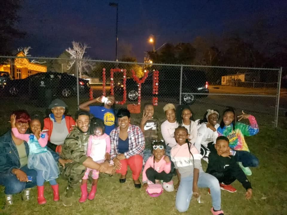 Large community group at night in front of JOY spelled in red cups