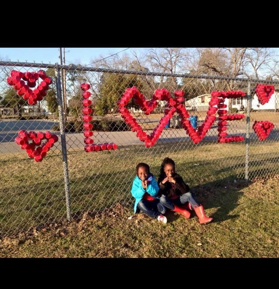 Two girls making heart shapes in front of LOVE spelled in red cups
