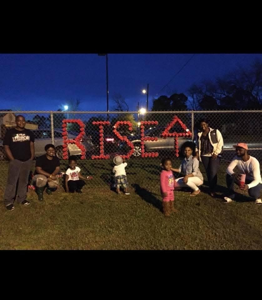 Community group at night in front of RISE and an upward arrow in red cups