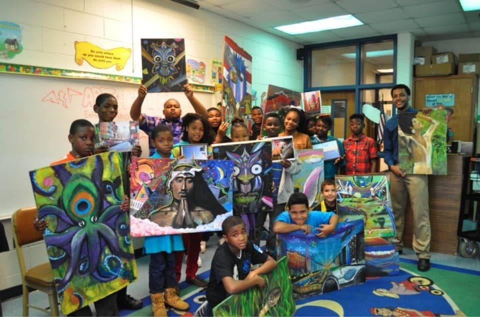 Youth art class - students and instructor holding finished canvases in a classroom.